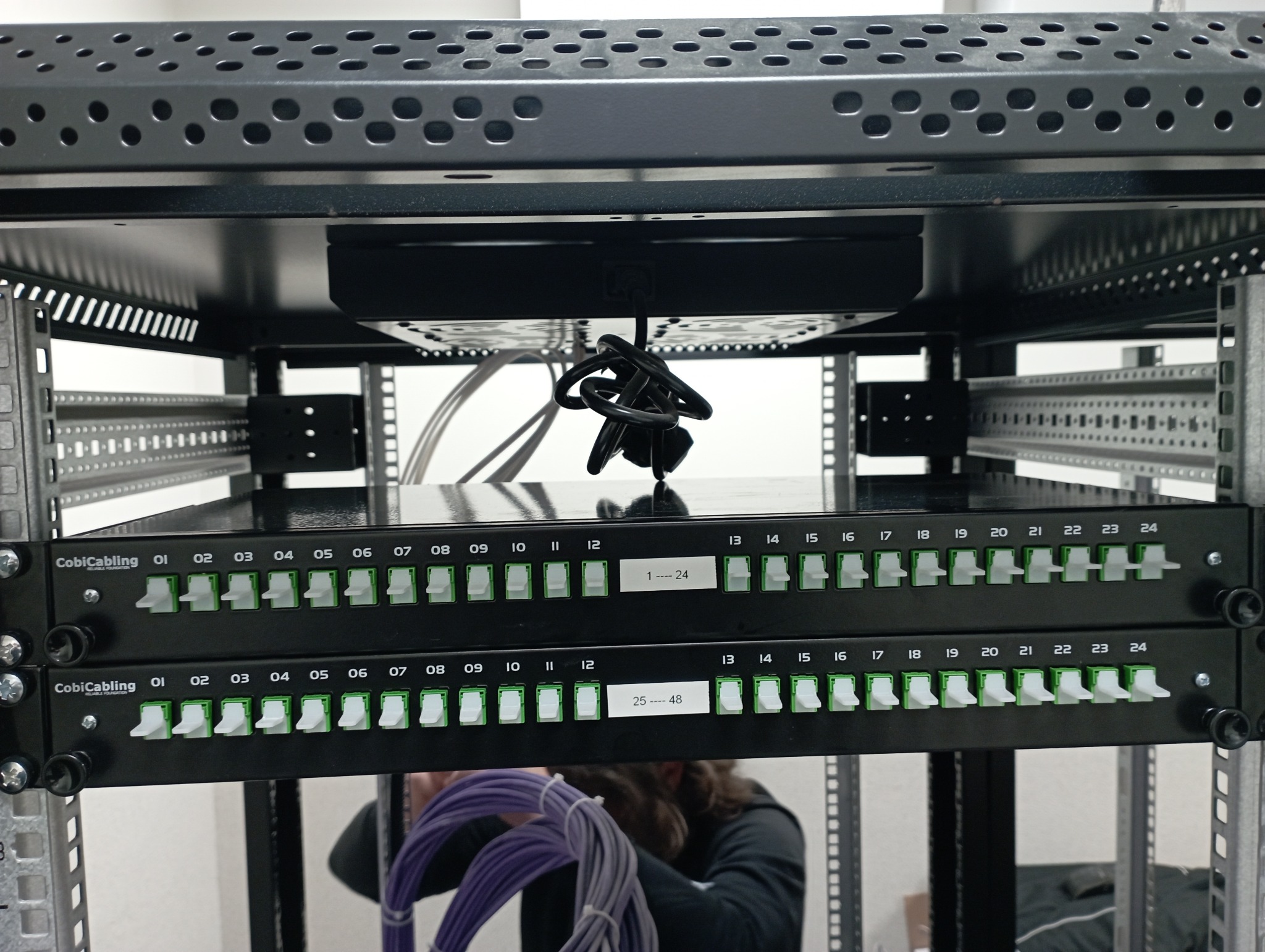 Patch panel w szafie rack, z widocznymi portami oznaczonymi numerami 1-48, kabel sieciowy w tle, widok z bliska.