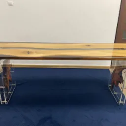 Stół z blatem z drewna i żywicy epoksydowej, z nogami z akrylu i wkomponowanymi kawałkami drewna, ustawiony na granatowym dywanie.