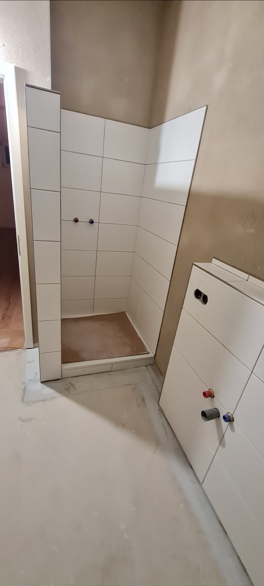 Płytki ścienne ułożone w kabinie prysznicowej, widoczne przyłącza wodne i fragment podłogi przed wykończeniem.