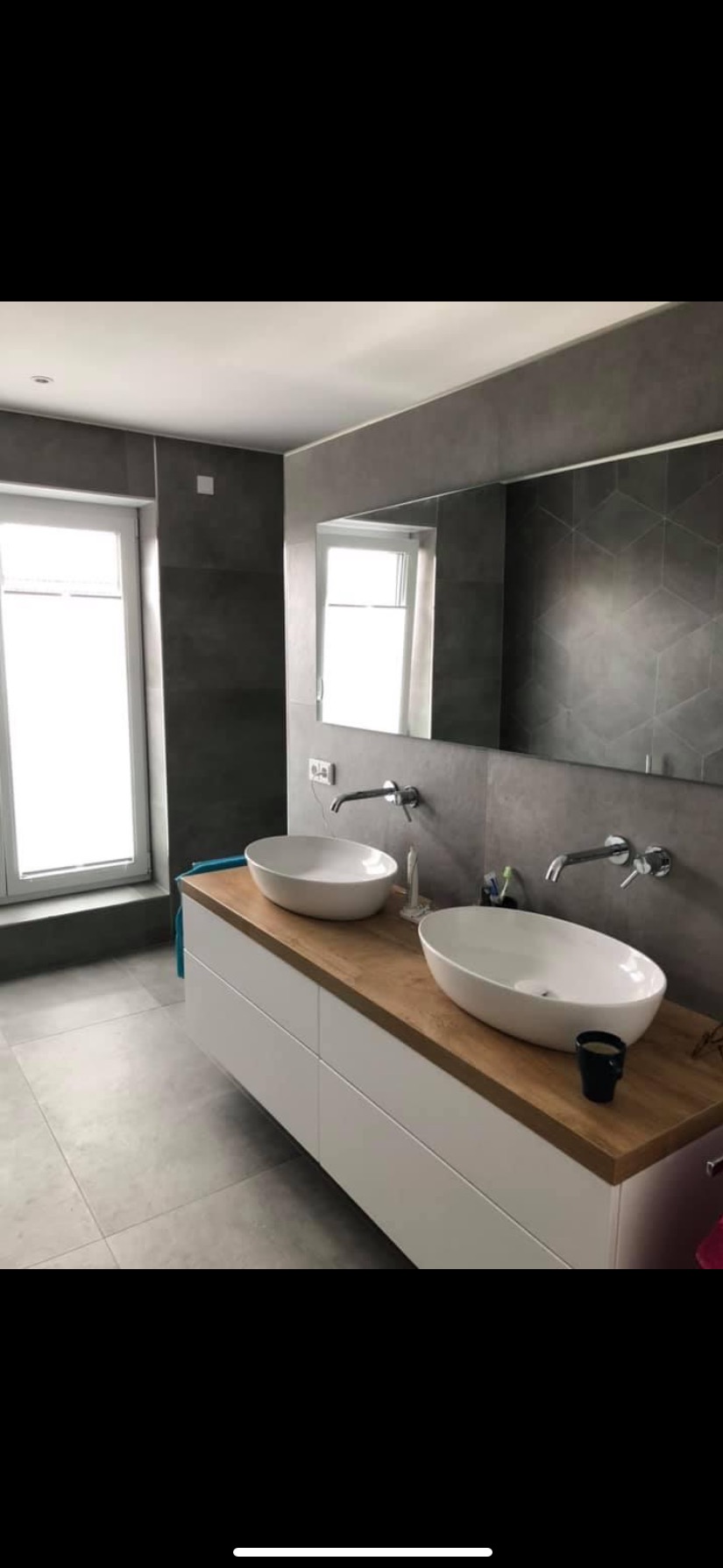 Nowoczesna łazienka z dwoma owalnymi umywalkami nablatowymi, drewnianym blatem, białymi szafkami i szarą płytką z geometrycznym wzorem na ścianie