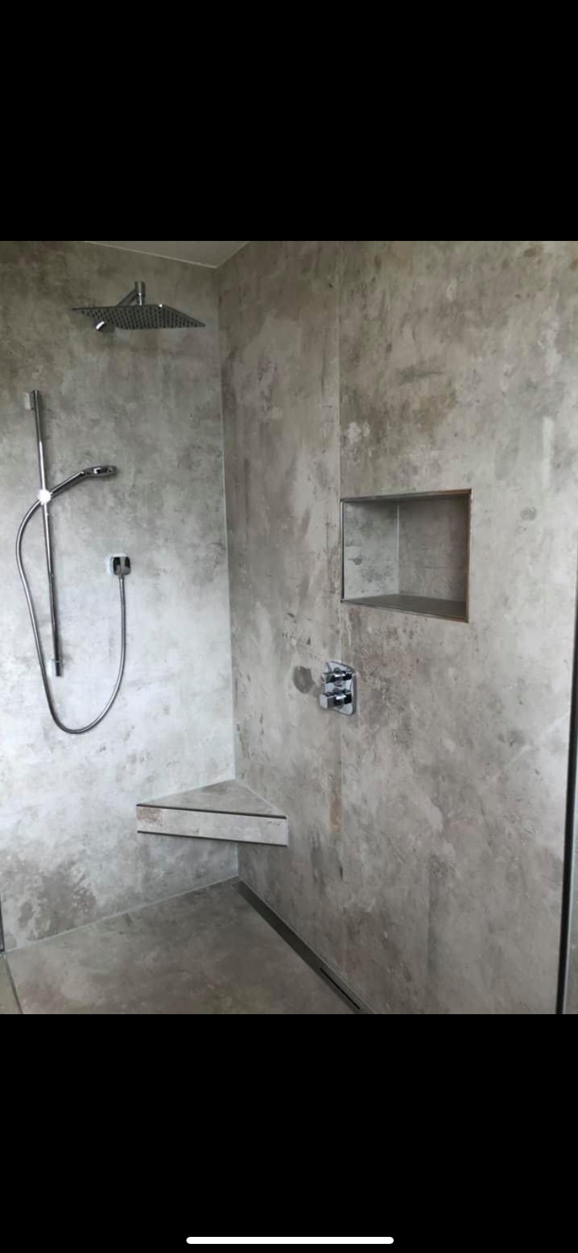 Wykończona kabina prysznicowa z szarymi ścianami imitującymi beton, chromowaną armaturą, półką narożną i wnęką w ścianie.