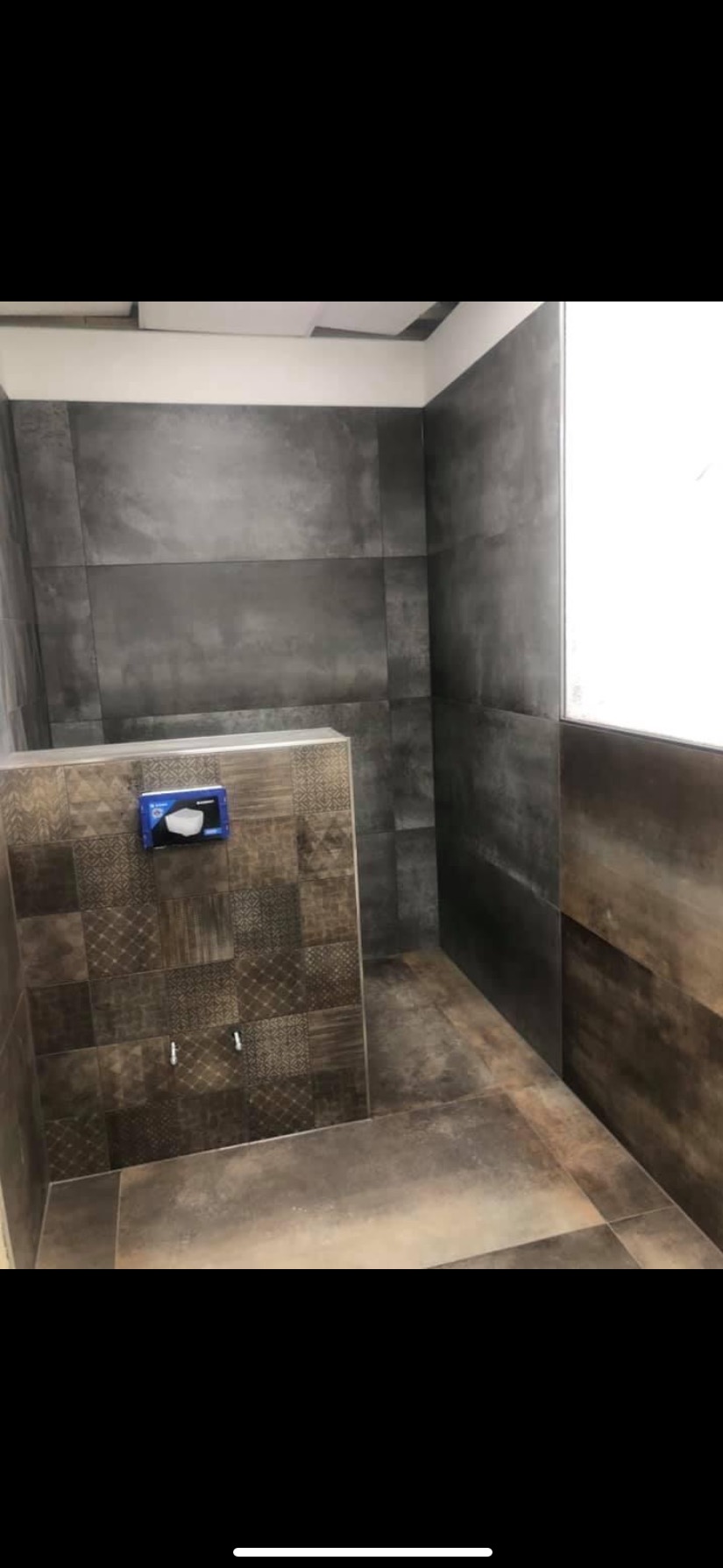 Wykończona łazienka z ciemnymi, matowymi płytkami imitującymi beton na ścianach i podłodze, oraz mozaiką na zabudowie stelaża WC, widoczna puszka instalacyjna pod przycisk spłukiwania.