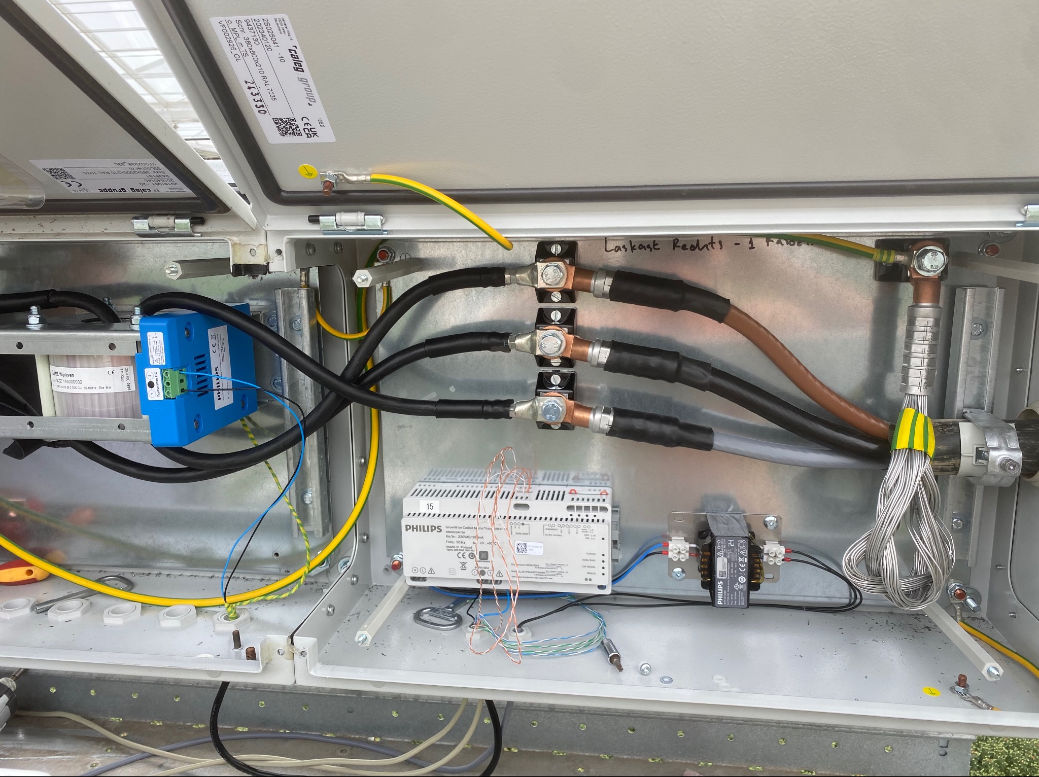 Otwarta skrzynka elektryczna z widocznymi elementami instalacji: przewodami, transformatorami Philips, zaciskami i elementami montażowymi, z napisem 'Laskast Rechts - 1 Farbe' na wewnętrznej ściance.