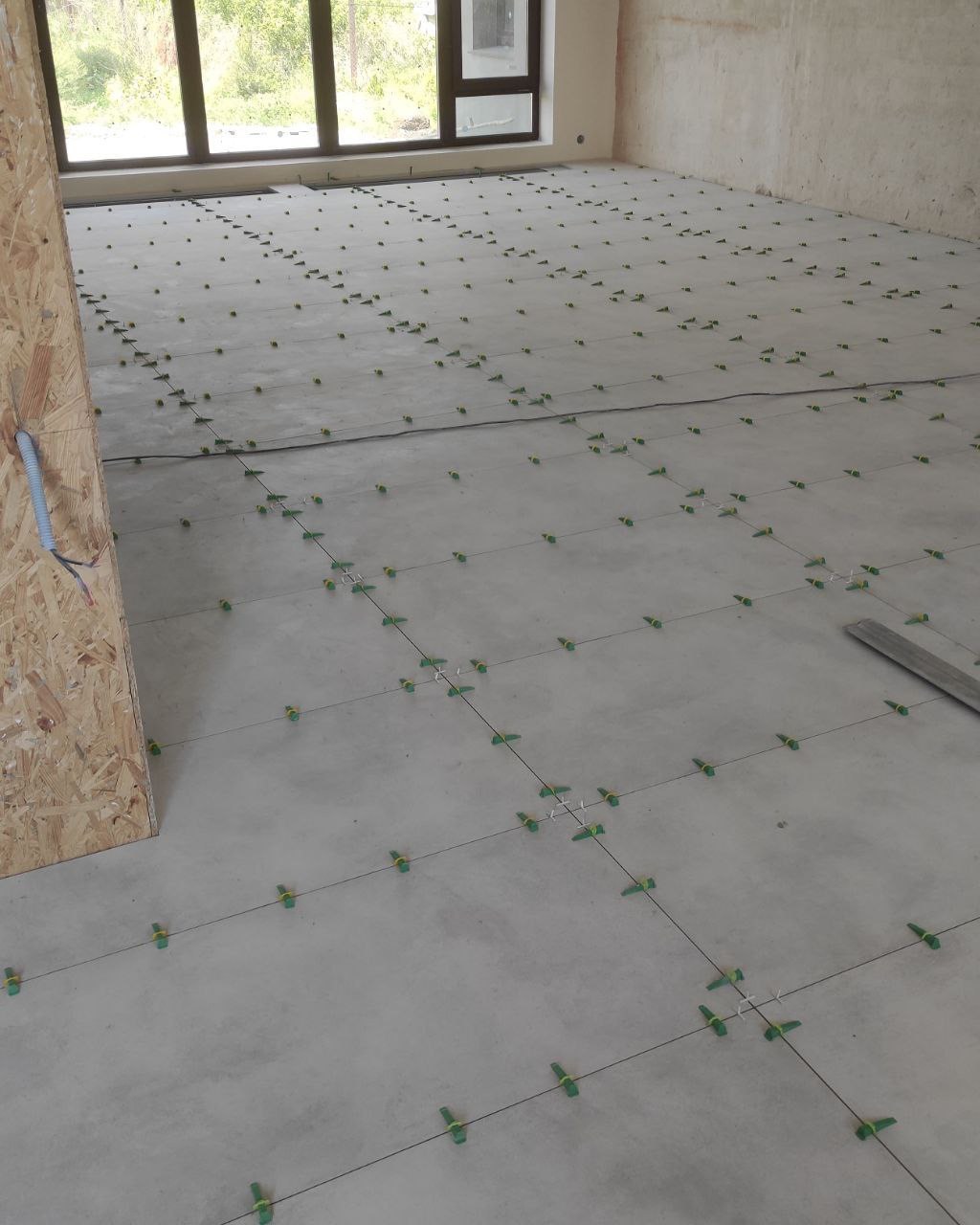 Układanie płytek podłogowych z użyciem systemu poziomowania w nowym mieszkaniu w Warszawie, widoczne krzyżyki dystansowe i kliny.