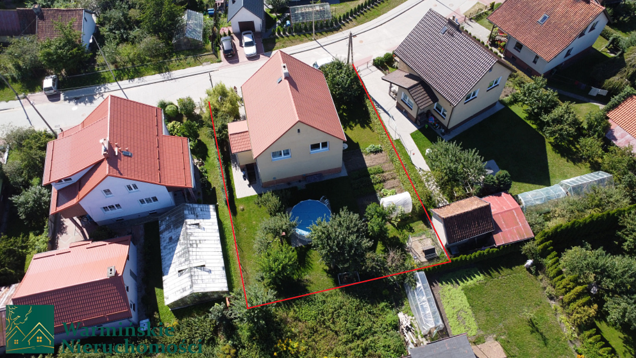 Zdjęcie z lotu ptaka przedstawiające dom jednorodzinny z ogrodem i basenem w Bartoszycach, granica działki oznaczona czerwoną linią.