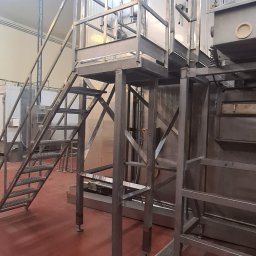 ARZO-SPAW - Metalowa konstrukcja platformy z schodami w hali przemysłowej, widoczne rury wentylacyjne i kratka ściekowa w posadzce.