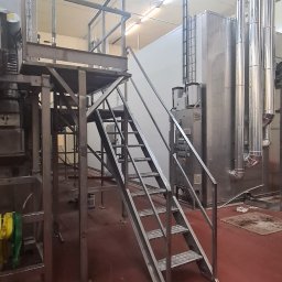 ARZO-SPAW - Metalowa konstrukcja schodów z platformą w hali przemysłowej, widoczne rury i maszyny w tle.