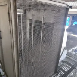 Metalowa obudowa z siatką ochronną, zamontowana na konstrukcji kratownicowej pod zadaszeniem, widoczne elementy mocujące.