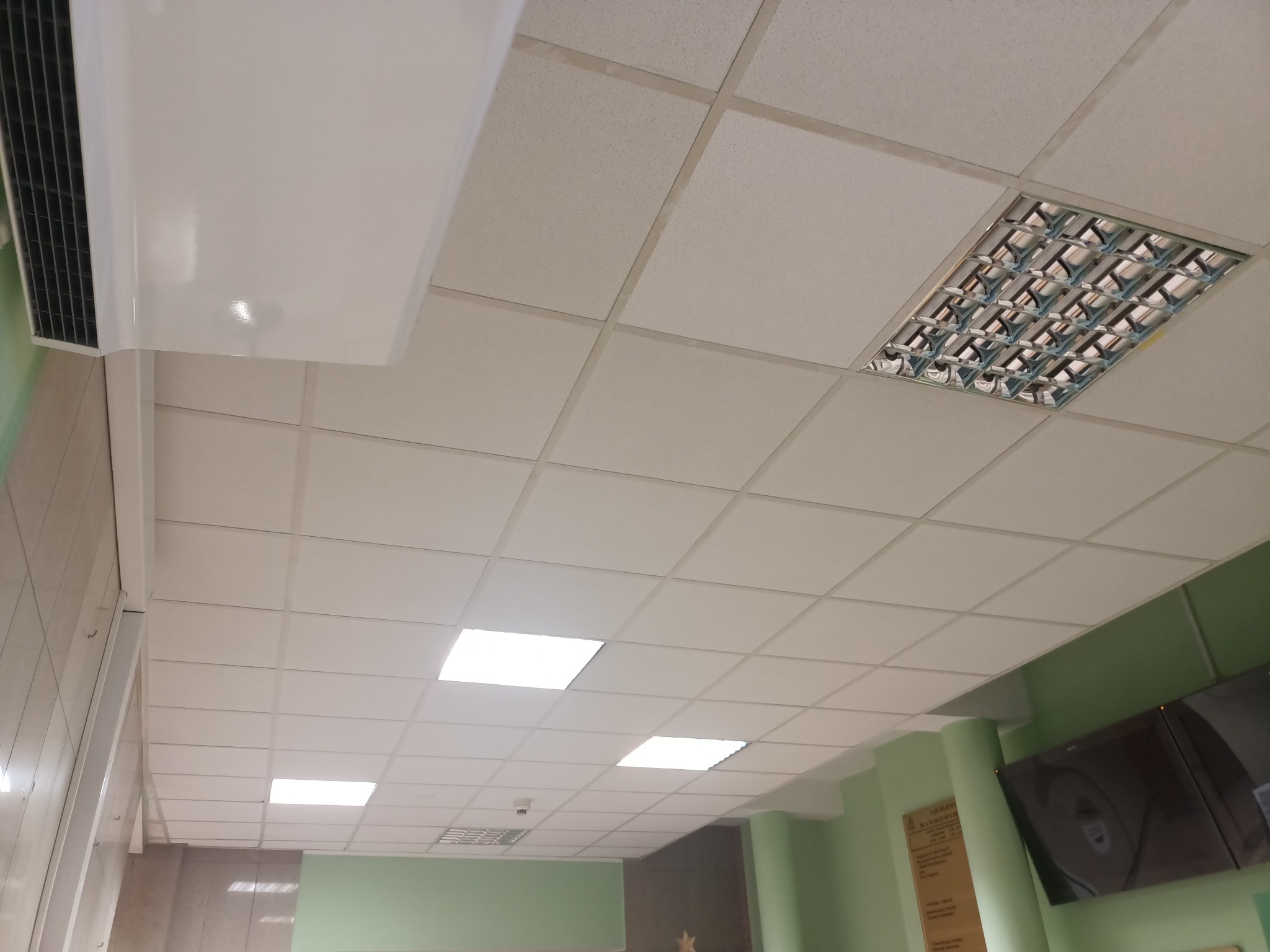 Kasetonowy sufit podwieszany z rastrową oprawą oświetleniową i nawiewnikiem klimatyzacji w pomieszczeniu biurowym z zielonymi ścianami.