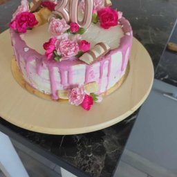 Smacznego-Domowego Jarosław Smażyk - Tort urodzinowy z różowym lukrem, kwiatami i świeczkami w kształcie liczby 30, umieszczony na drewnianym talerzu na tle marmurowego blatu.