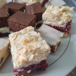 Smacznego-Domowego Jarosław Smażyk - Różnorodne ciasta na białym talerzu z delikatnym złotym obramowaniem. Wśród nich wyróżniają się ciasta z kremem, owocami i czekoladową polewą.