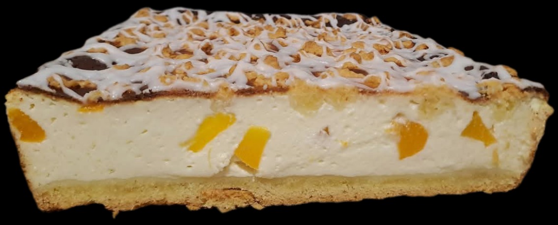 Kawałek sernika z brzoskwiniami, polany czekoladą, białym lukrem i posypany orzechami na czarnym tle. Widoczny przekrój ciasta.