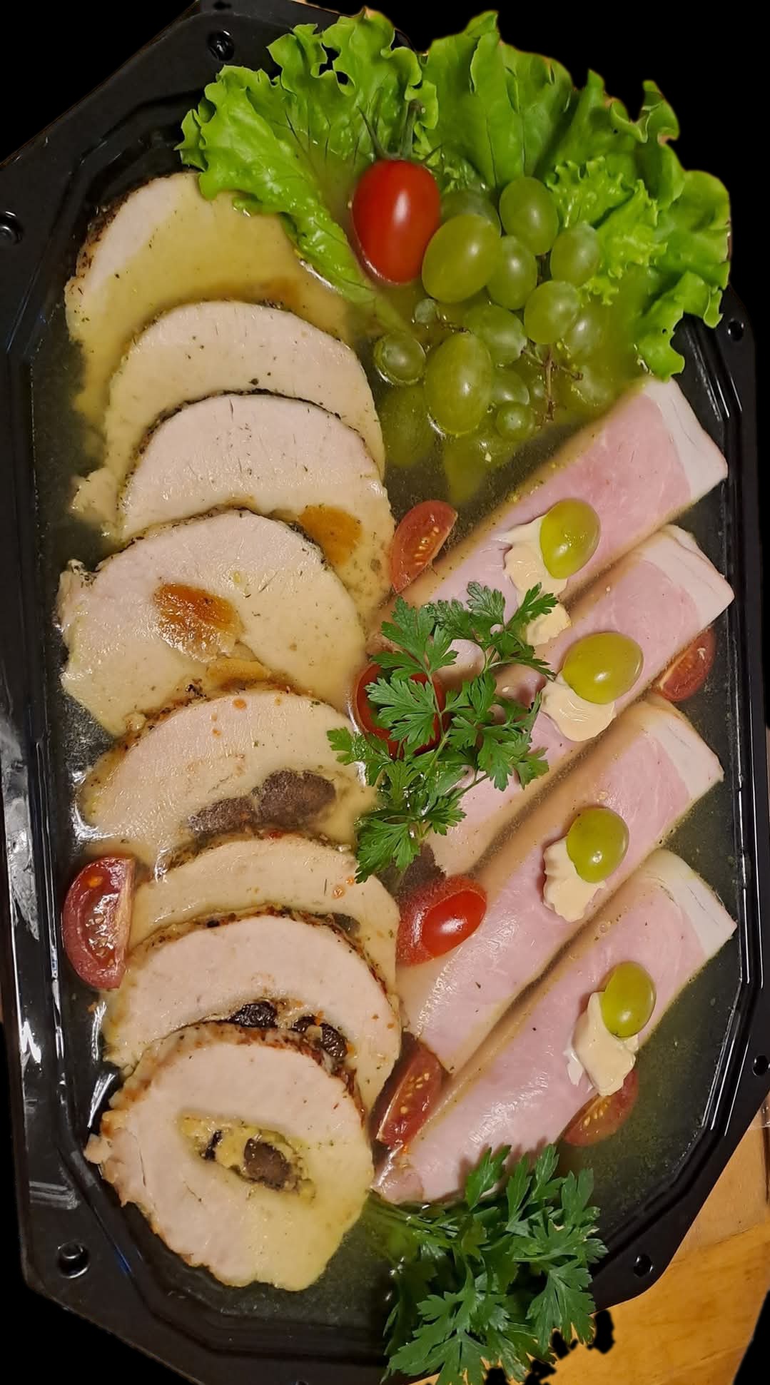 Elegancka kompozycja w czarnym pojemniku: roladki z nadzieniem, szynka z kremem i winogronami, pomidorki koktajlowe i zielenina. Gotowa propozycja na przyjęcie.