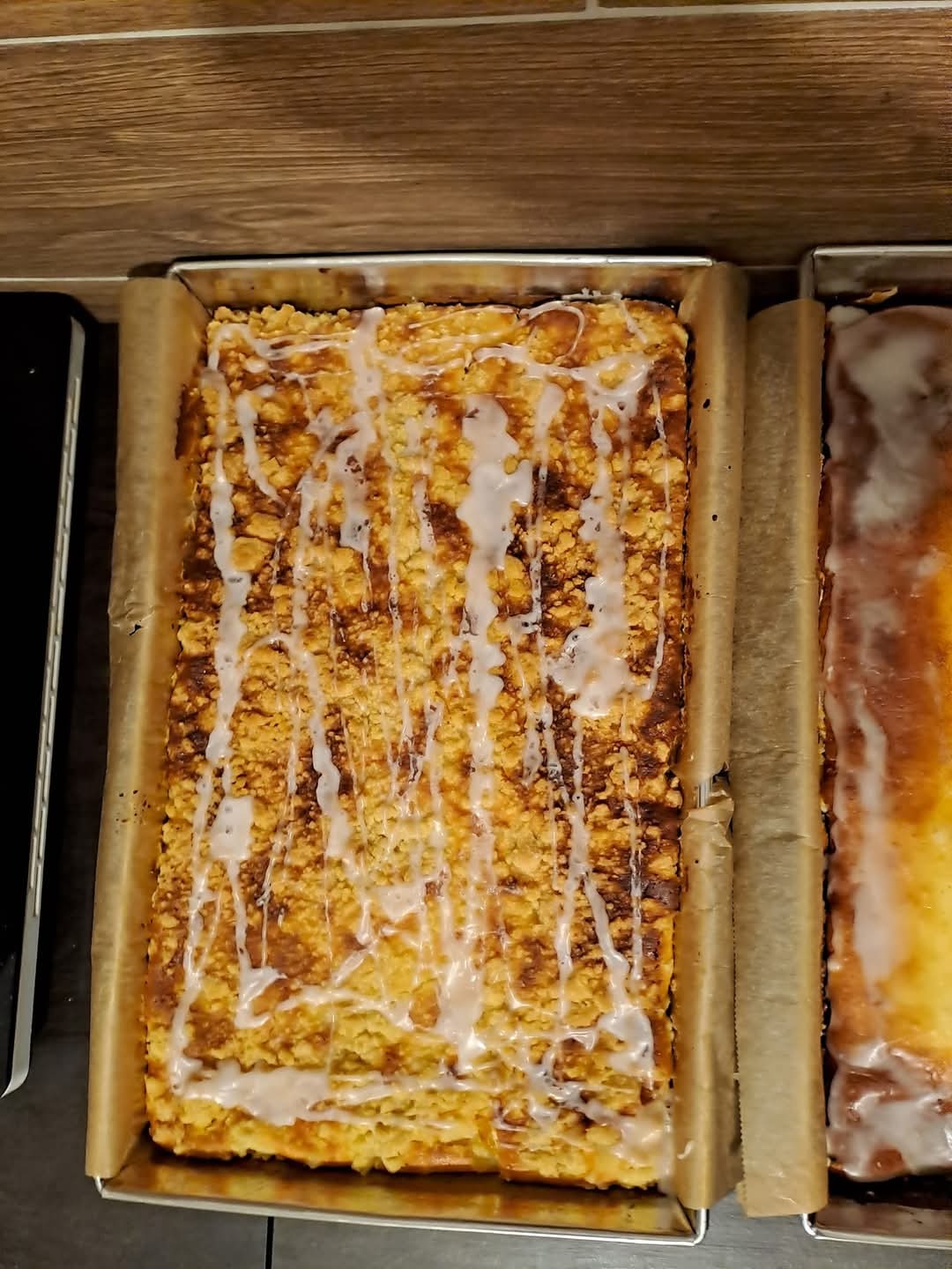 Kruche ciasto z lukrem w blaszce, widoczne z góry, obok ciasto cytrynowe. Domowe wypieki na papierze do pieczenia, gotowe do podania.