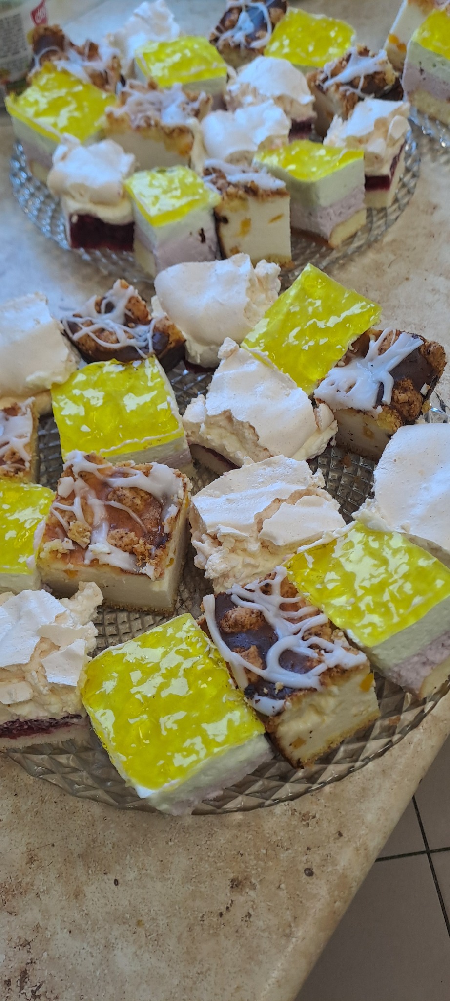 Szklany talerz z różnorodnymi, apetycznymi ciastami w kształcie kwadratów, z galaretką, bezą i kremem, idealne na słodki poczęstunek.