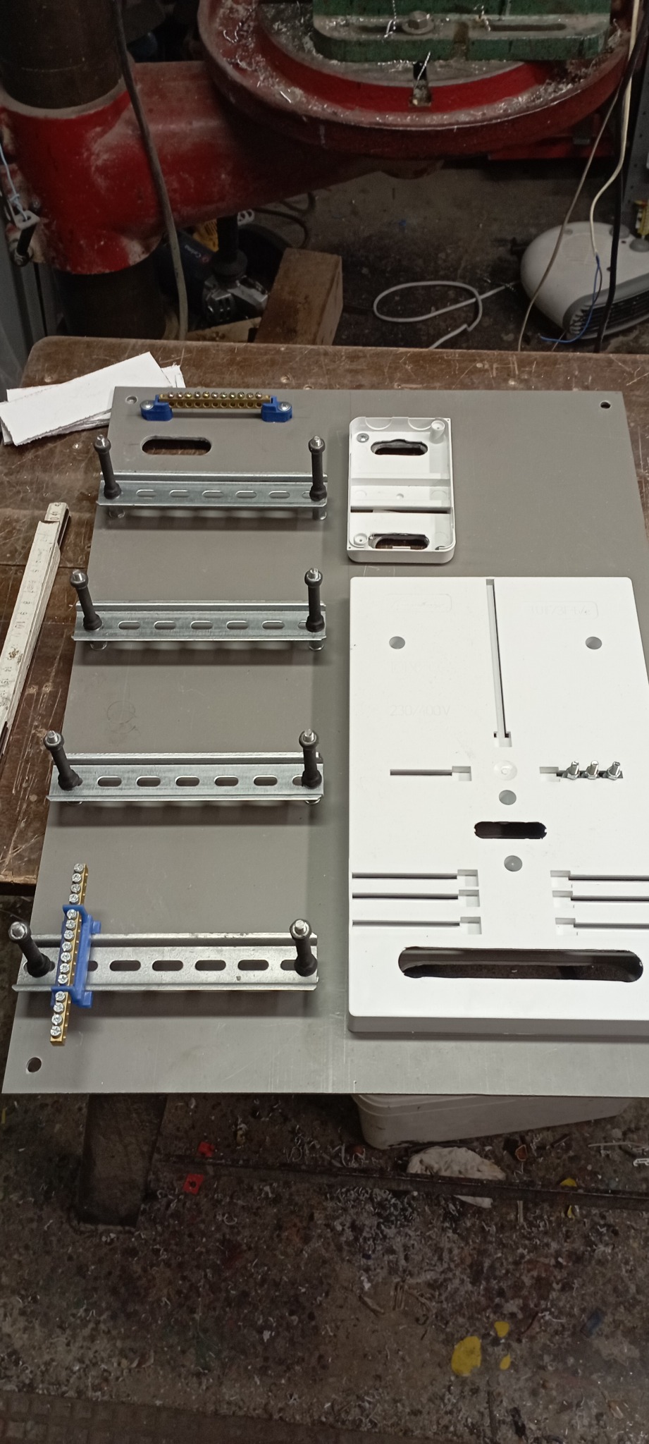 Przygotowany panel montażowy z szynami DIN, listwą zaciskową i obudową, ułożony na roboczym stole.