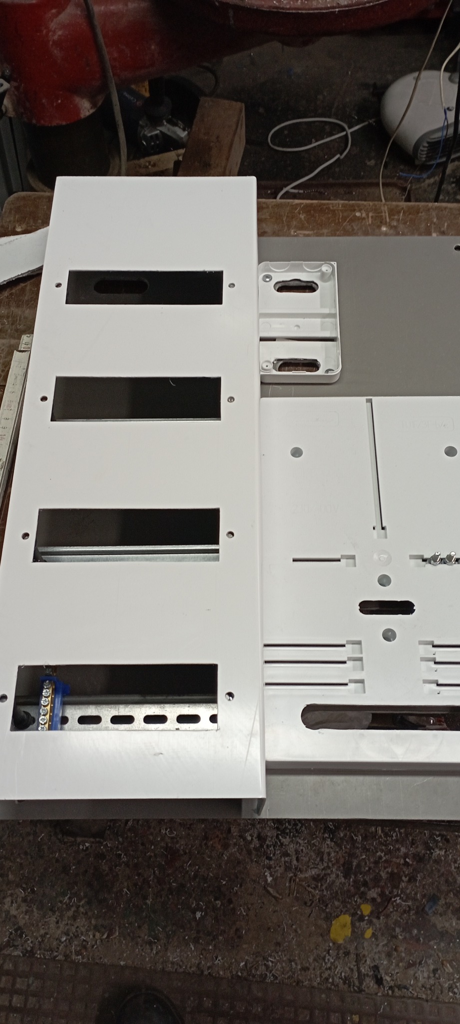 Rozdzielnica elektryczna, biała obudowa z otworami na moduły, widoczna listwa DIN i zaciski, na roboczym stole.