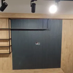 Nowoczesna zabudowa ściany z drewnopodobną okładziną, czarnymi lamelami i metalowym regałem z półkami, oświetlenie punktowe.