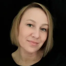 Portret uśmiechniętej kobiety z krótkimi blond włosami i zielonymi oczami na czarnym tle.