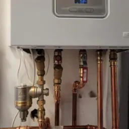 Nowoczesny piec gazowy z podłączeniem miedzianych rur i zaworów, widoczny filtr magnetyczny na przewodzie.