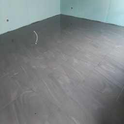 Usługi ogólnobudowlane Bartłomiej Jakubiak - Ułożona szara glazura imitująca kamień na podłodze w pomieszczeniu z płytami gipsowo-kartonowymi na ścianach we Wrocławiu, widoczny wystający kabel elektryczny.