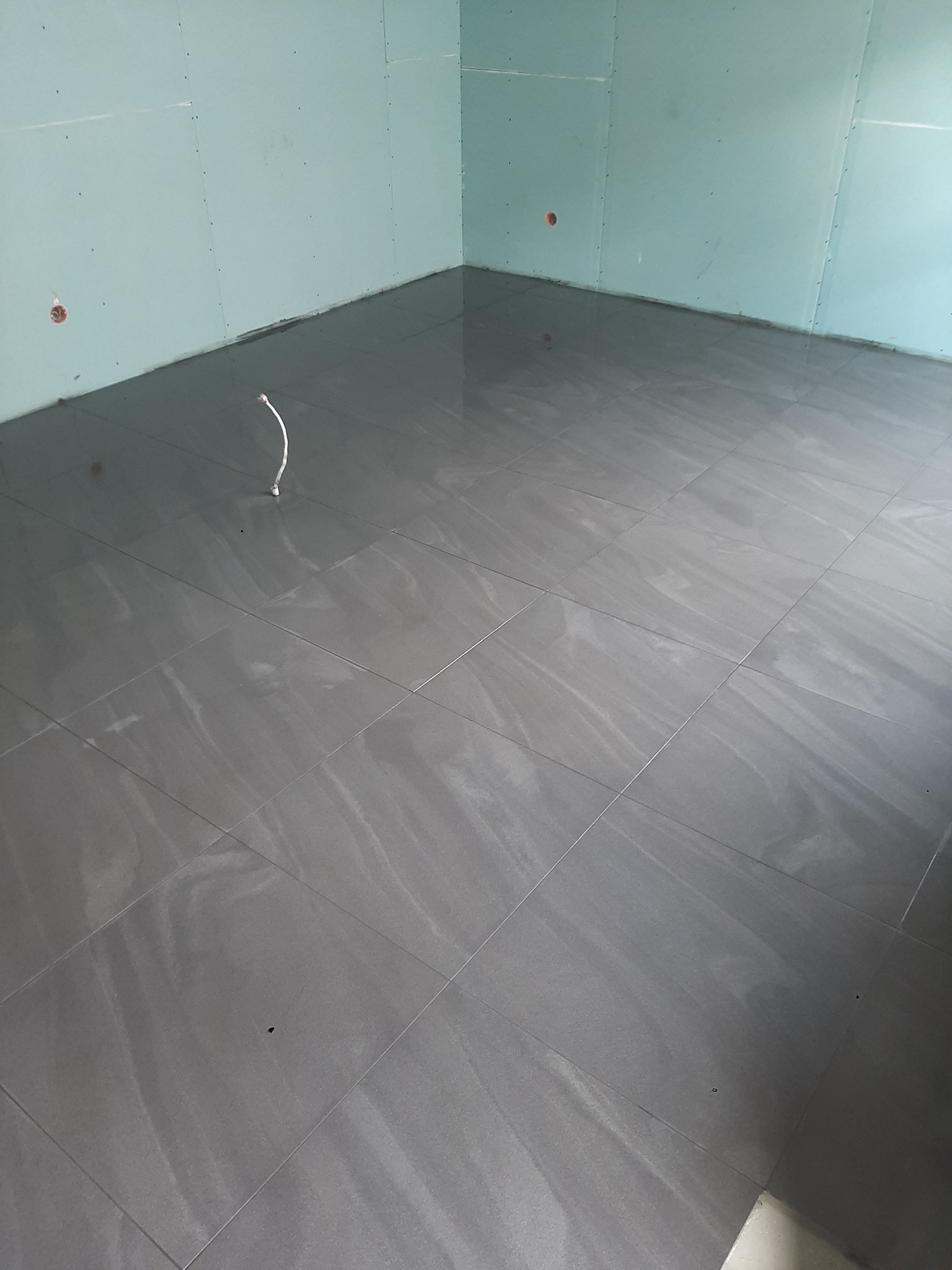 Ułożona szara glazura imitująca kamień na podłodze w pomieszczeniu z płytami gipsowo-kartonowymi na ścianach we Wrocławiu, widoczny wystający kabel elektryczny.