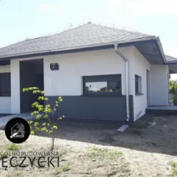 Nowoczesny dom jednorodzinny z szarą elewacją i dachem, widoczny numer domu '7', logo firmy budowlanej w rogu zdjęcia.