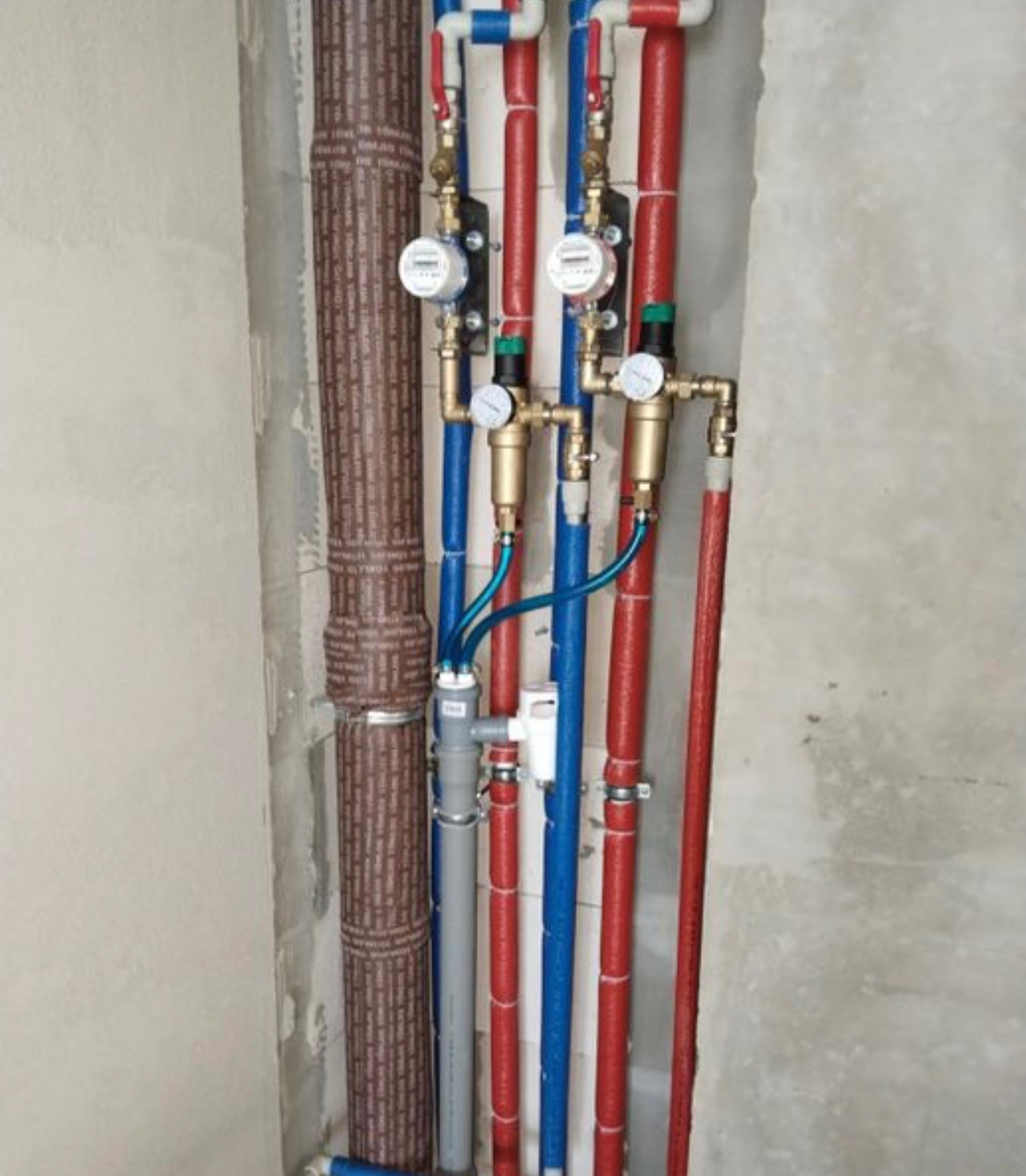 Instalacja wodna z licznikami i rurami w izolacji, wykonana w trakcie remontu w Warszawie. Widoczne elementy miedziane i plastikowe.