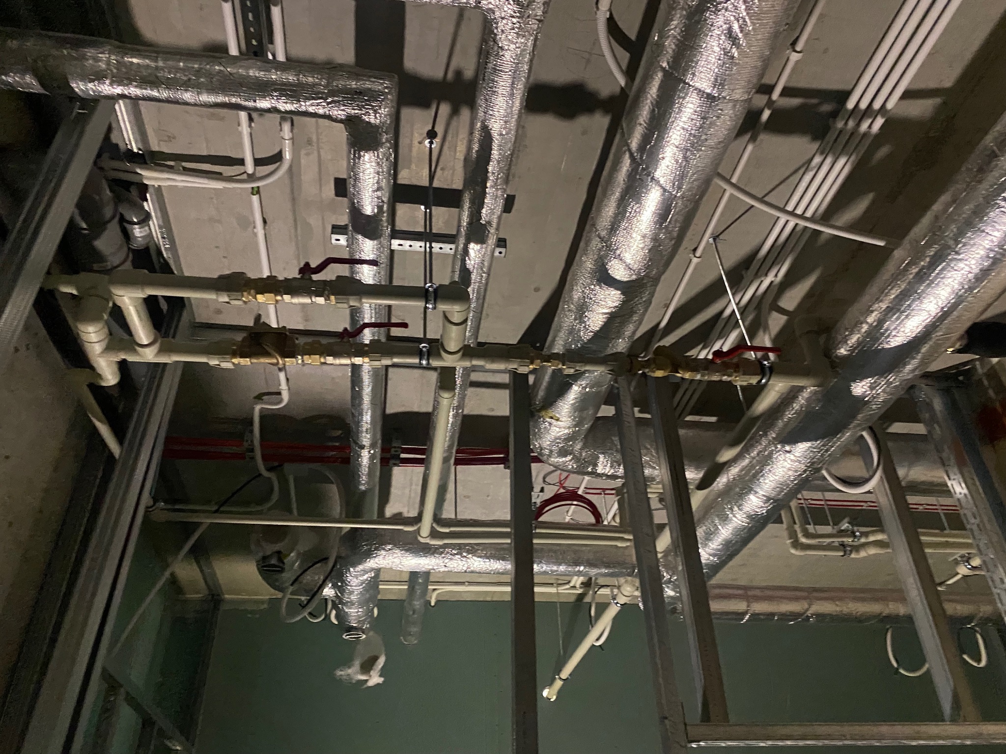 Instalacja rur i przewodów pod sufitem w trakcie remontu. Widoczne rury izolowane, rury PCV, przewody elektryczne i metalowa konstrukcja szkieletowa.