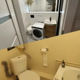 Porównanie dwóch łazienek: górna po remoncie w bieli z pralką, umywalką na szafce i dekoracyjnymi trawami w wazonie, dolna w odcieniach beżu z widoczną toaletą, rurami i wanną.