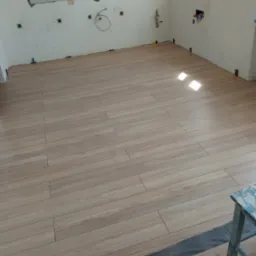 Ułożona podłoga z paneli imitujących drewno w trakcie remontu łazienki, widoczne przygotowane ściany pod płytki i instalacje, oraz resztki opakowania paneli podłogowych Kronostep flooring.