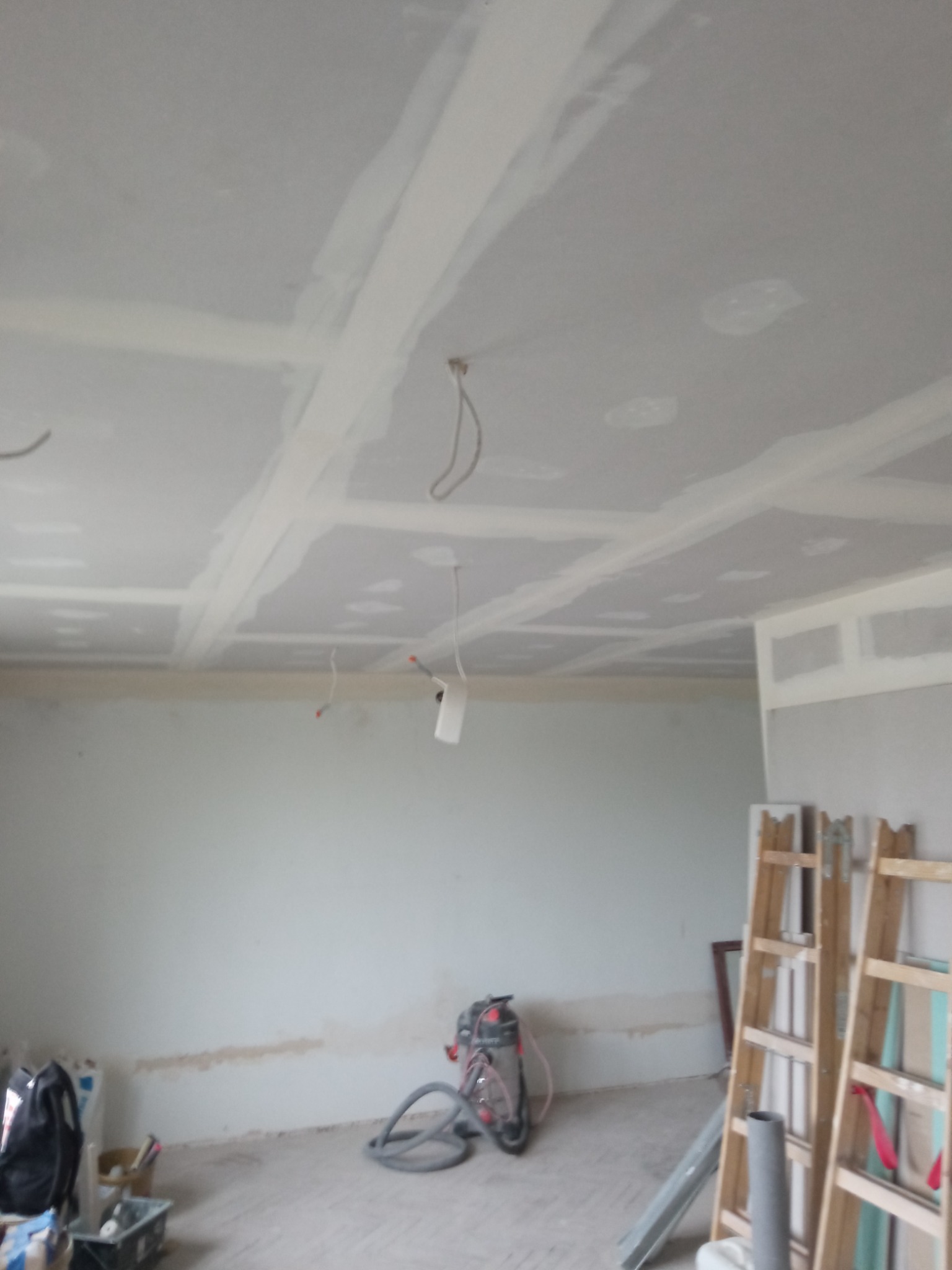 Wnętrze w trakcie prac wykończeniowych: sufit z płyt gipsowo-kartonowych ze spoinami wzmocnionymi taśmą i pokrytymi masą szpachlową, widoczne przewody elektryczne, odkurzacz przemysłowy...