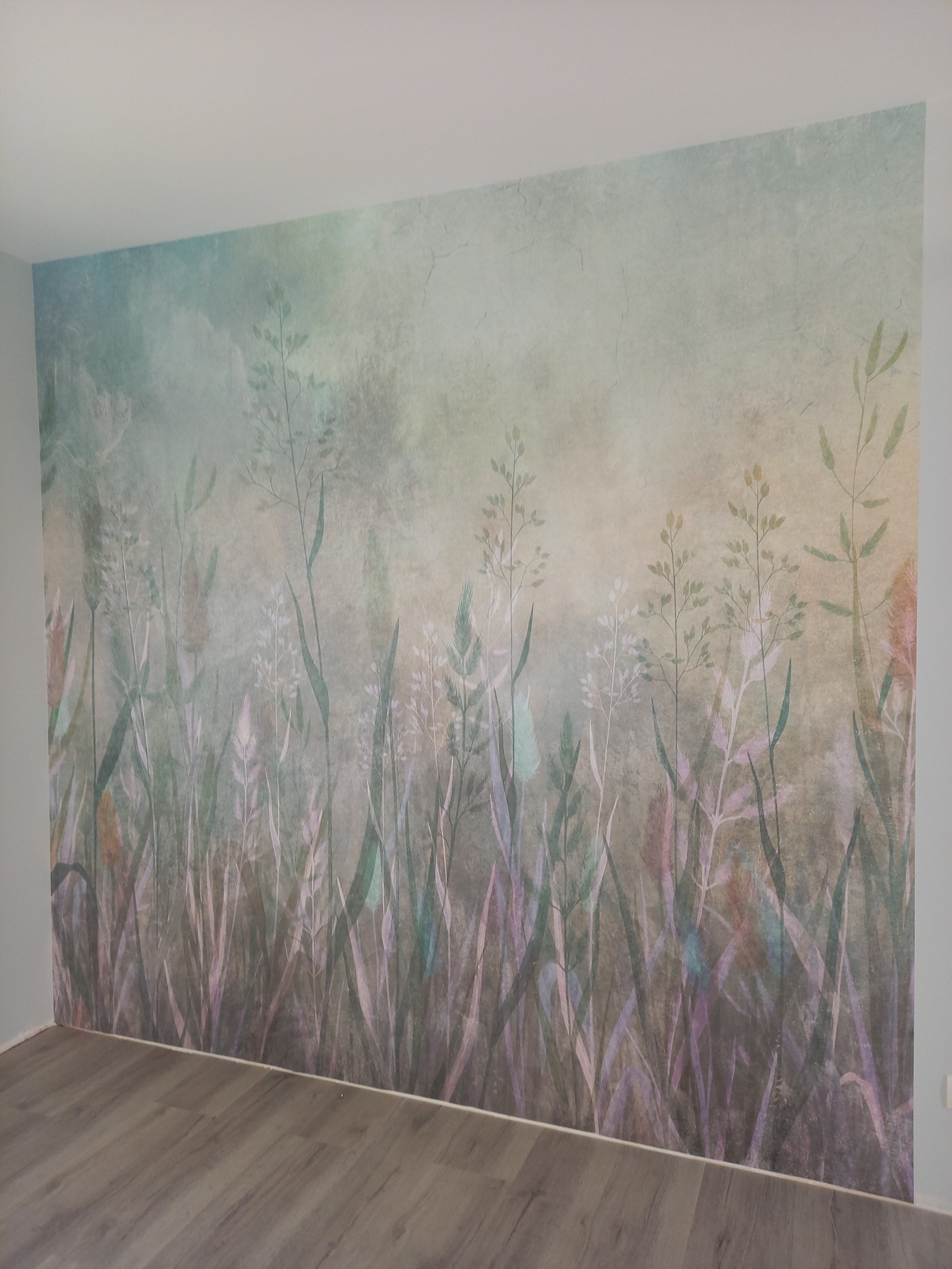 Ściana z tapetą w pastelowe trawy i kwiaty, szare panele podłogowe, widok z dołu.