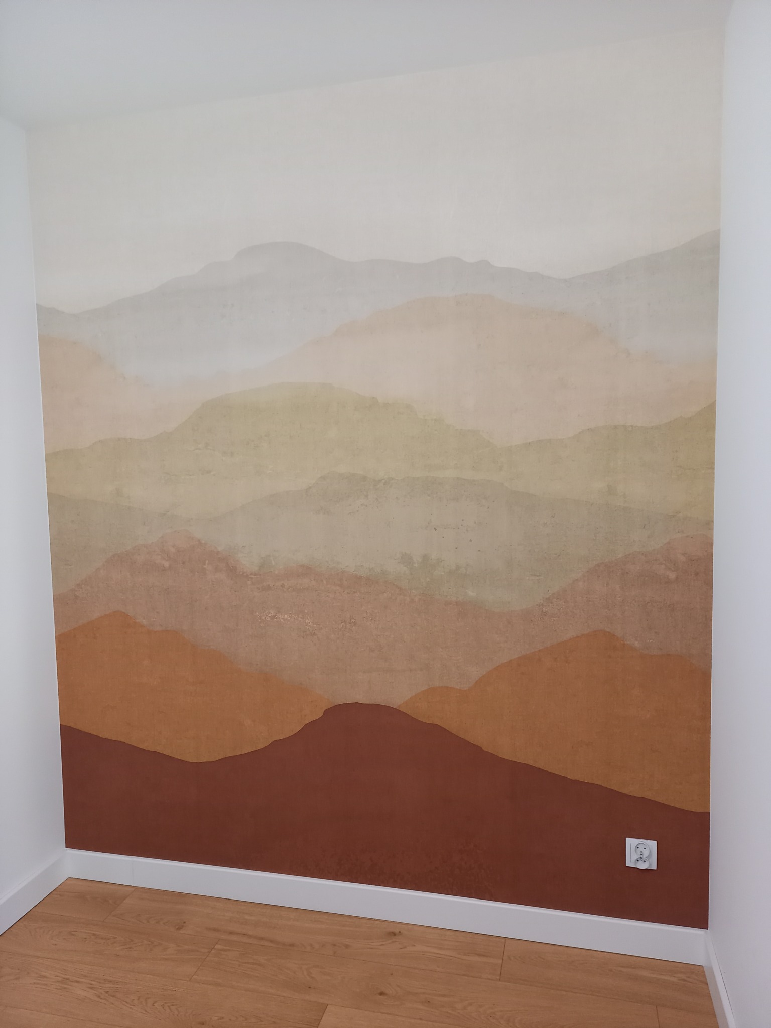 Ściana z ręcznie malowanym motywem górskim w odcieniach beżu, brązu i szarości, widoczna biała listwa przypodłogowa i drewniana podłoga