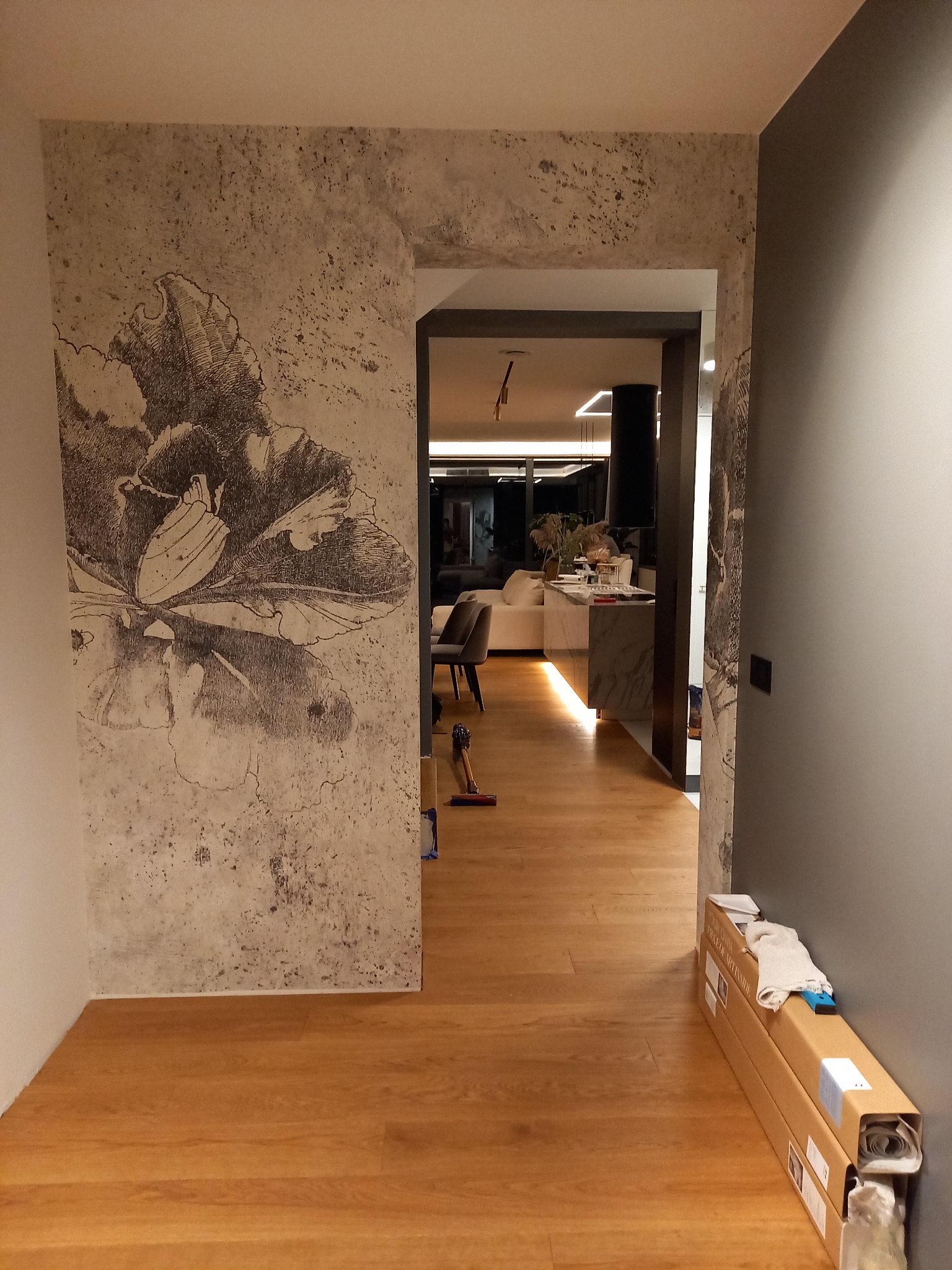 Wykończona ściana z efektem dekoracyjnym i motywem kwiatowym w nowoczesnym wnętrzu. Widoczne elementy wykończeniowe podłogi i przejście do innego pomieszczenia.