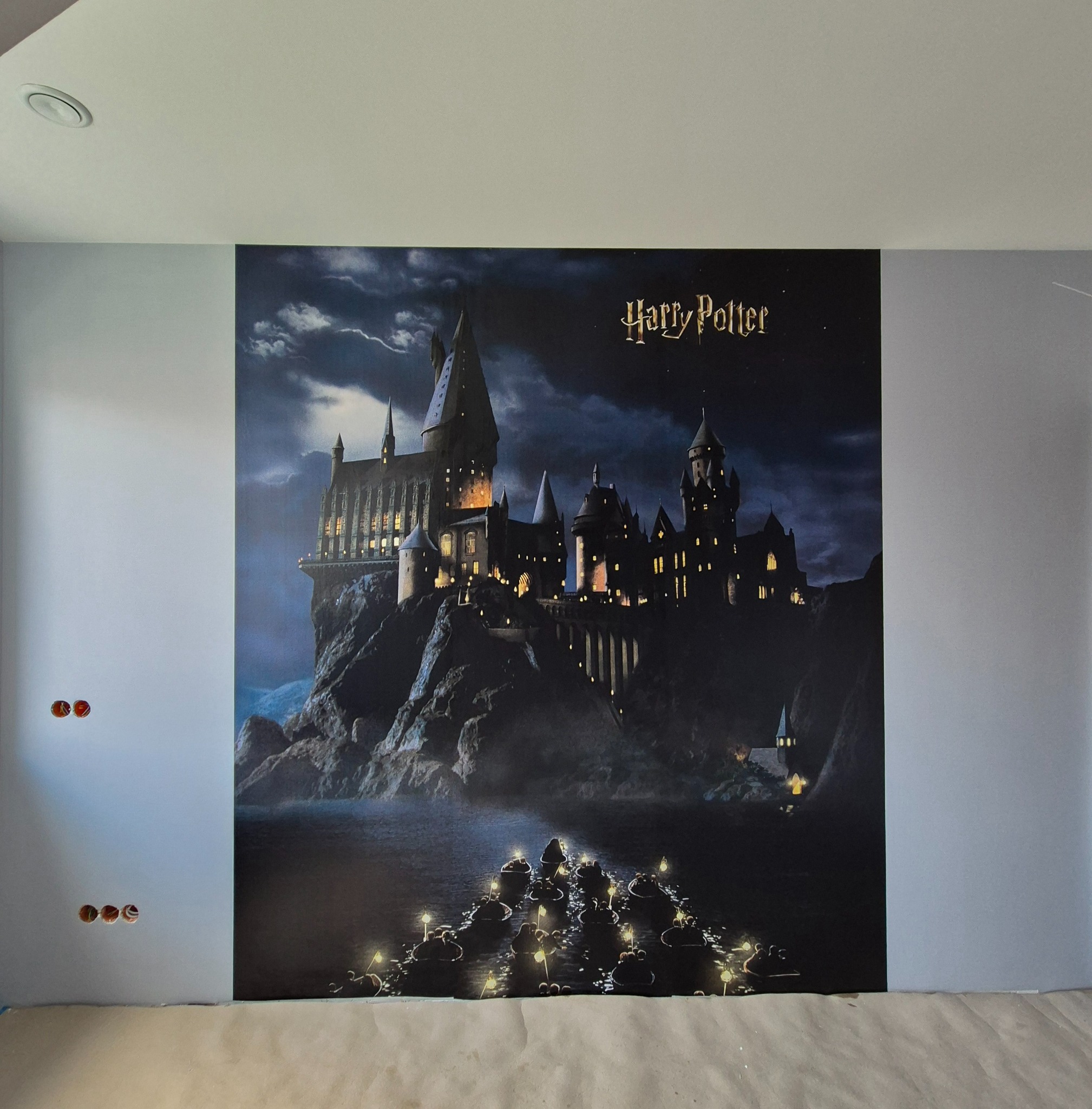 Ściana z tapetą przedstawiającą Hogwart. Widoczne niedokończone gniazdka elektryczne. Tapeta z motywem zamku z filmu Harry Potter.