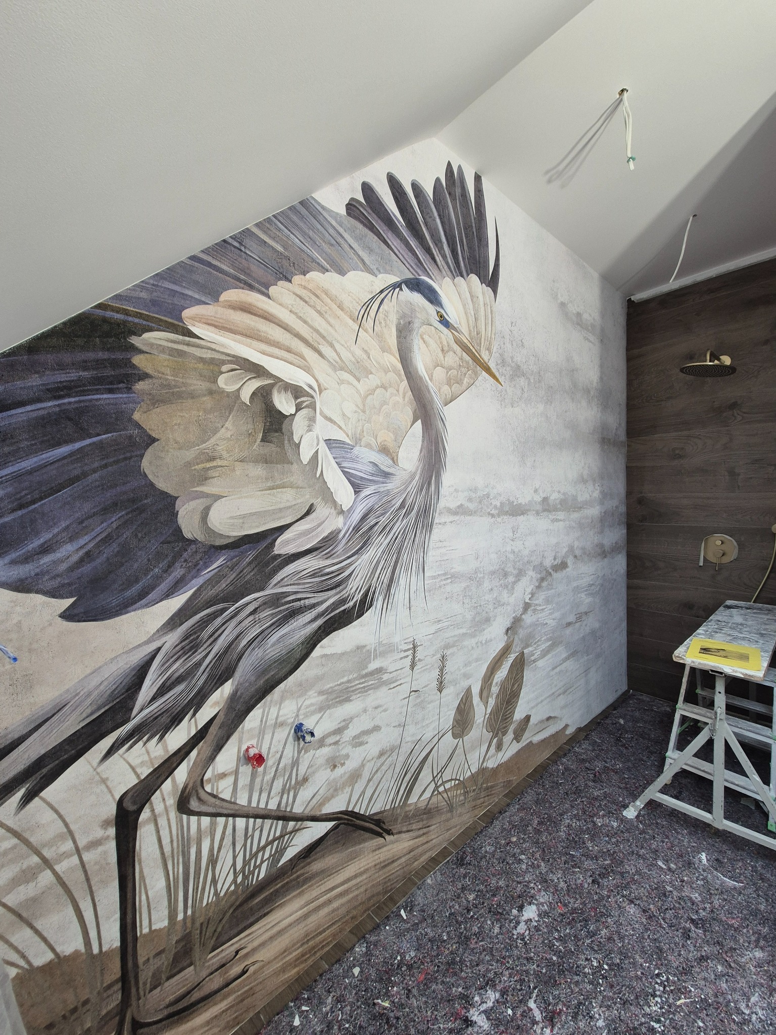 Tapeta z motywem czapli w łazience, widoczna drabina malarska i fragment prysznica. Dekoracja ścienna w trakcie prac wykończeniowych.