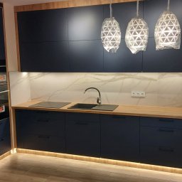 MEBS MARIUSZ SYC - Nowoczesna kuchnia z ciemnymi, matowymi frontami, drewnianym blatem, marmurową ścianą i trzema lampami wiszącymi w kształcie diamentów, jeszcze w folii ochronnej.