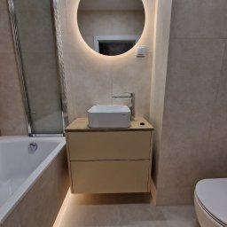 MEBS MARIUSZ SYC - Nowoczesna łazienka z podświetlanym lustrem, umywalką nablatową na szafce z dwiema szufladami i podświetleniem pod szafką, obok wanna z parawanem nawannowym.