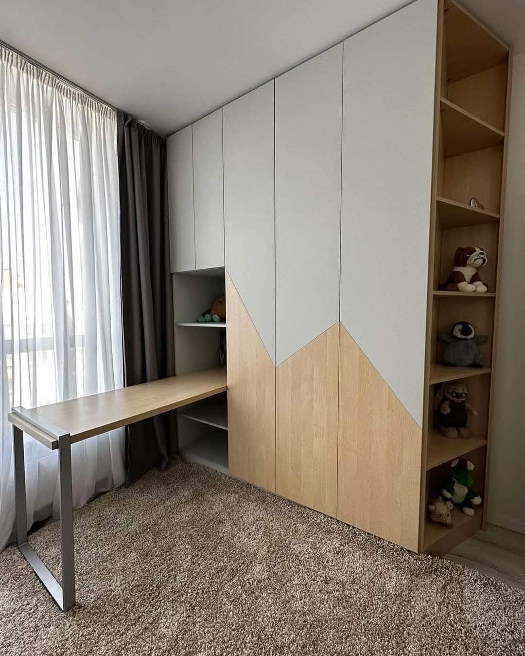 Biało-drewniana zabudowa meblowa z wysuwanym biurkiem i otwartymi półkami, uzupełniona o pluszowe zabawki jako dekoracja, na tle okna z zasłonami.