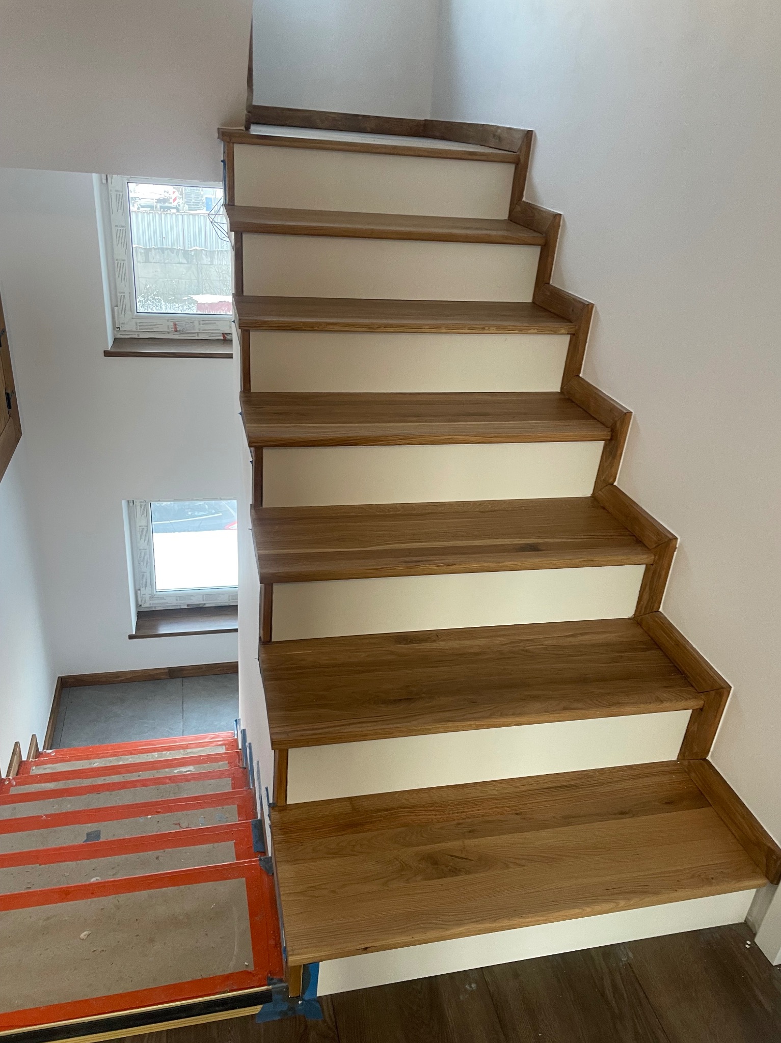 Drewniane schody z białymi podstopnicami, widok z góry, schody w trakcie montażu z zabezpieczeniem na dolnych stopniach.