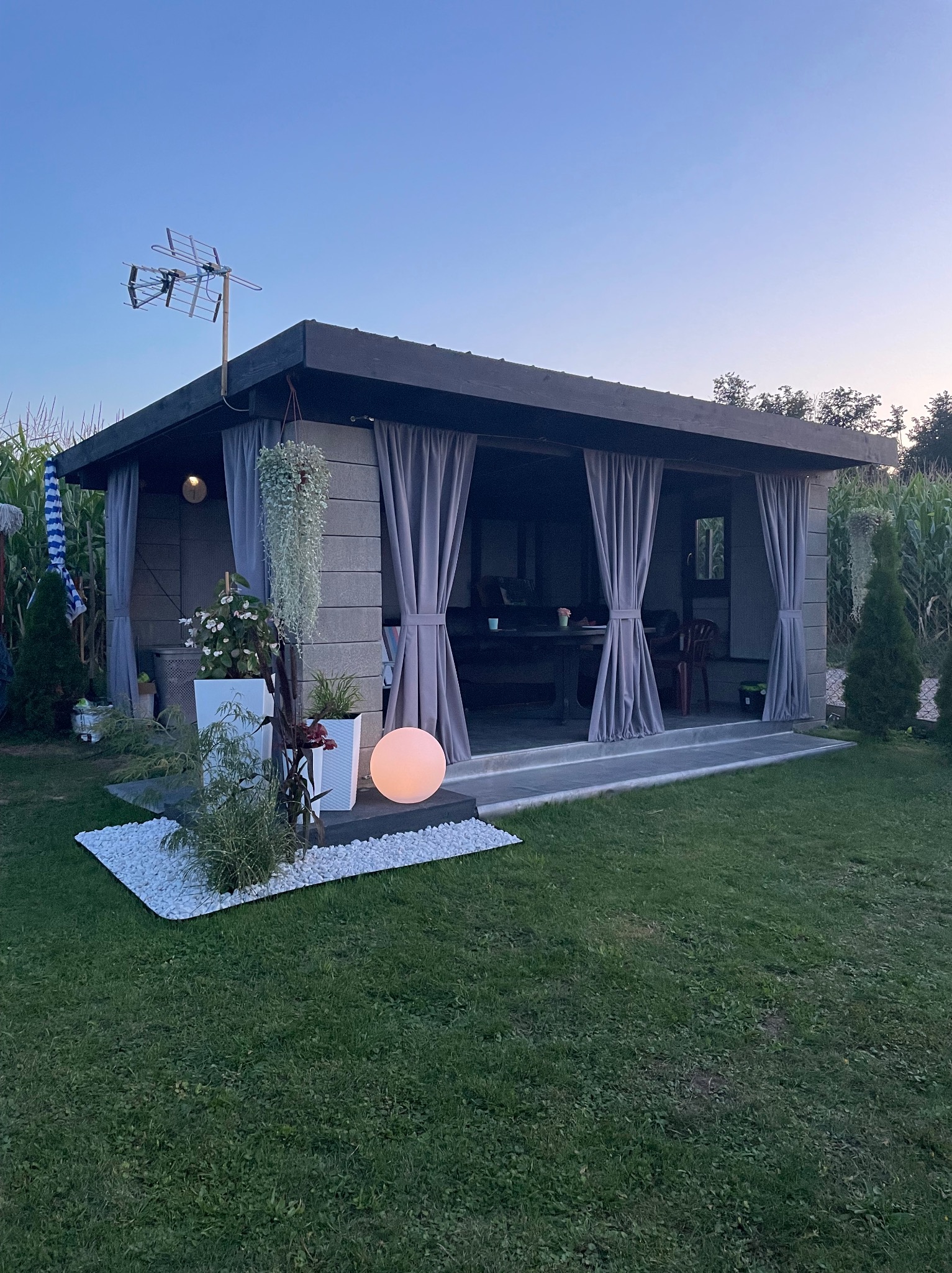 Altana z zasłonami w ogrodzie, oświetlona kulą, z anteną telewizyjną na dachu.