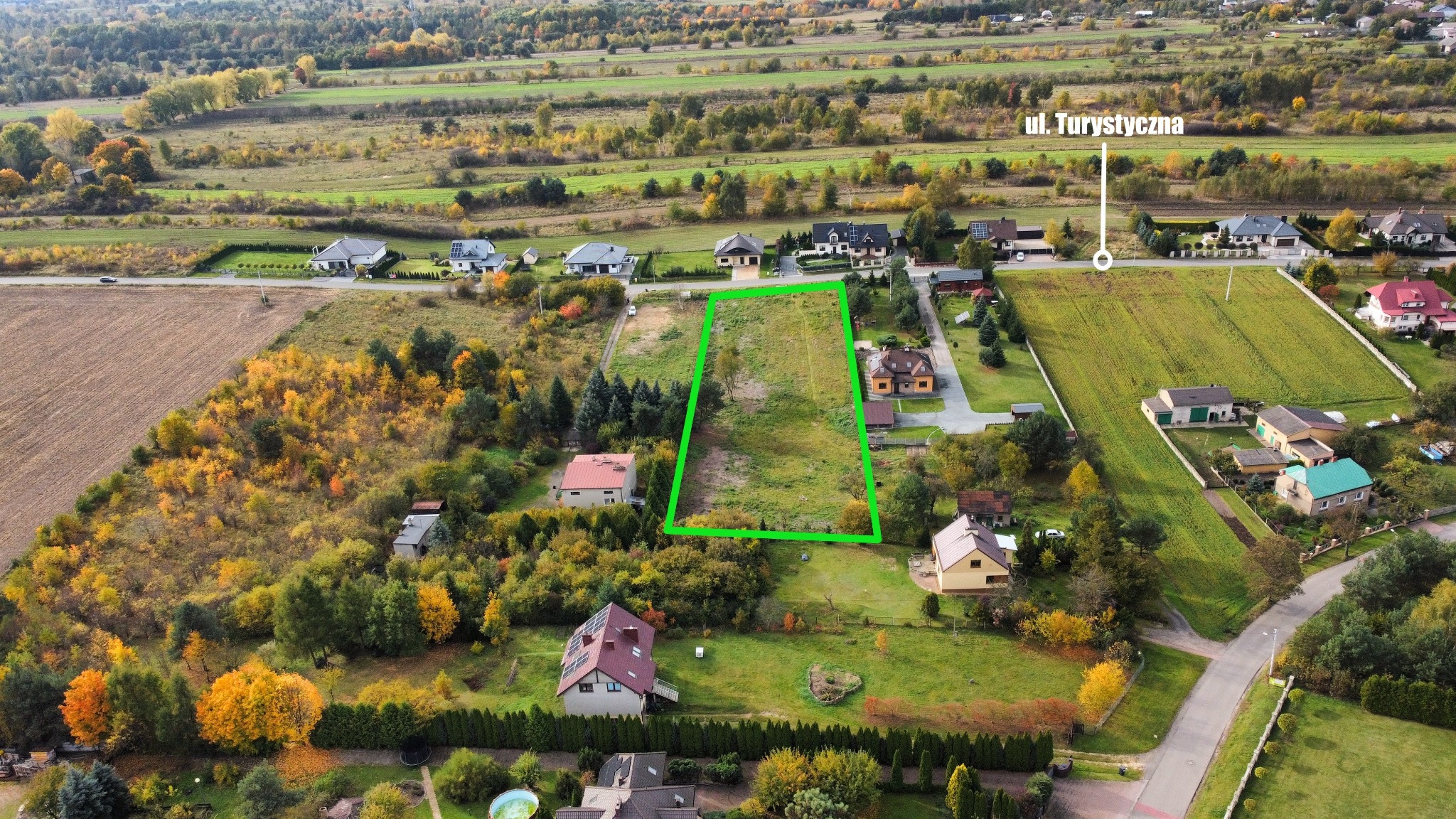 Działka budowlana z zielonym obrysem, widok z lotu ptaka na tereny podmiejskie w jesiennej scenerii, w tle ul. Turystyczna.