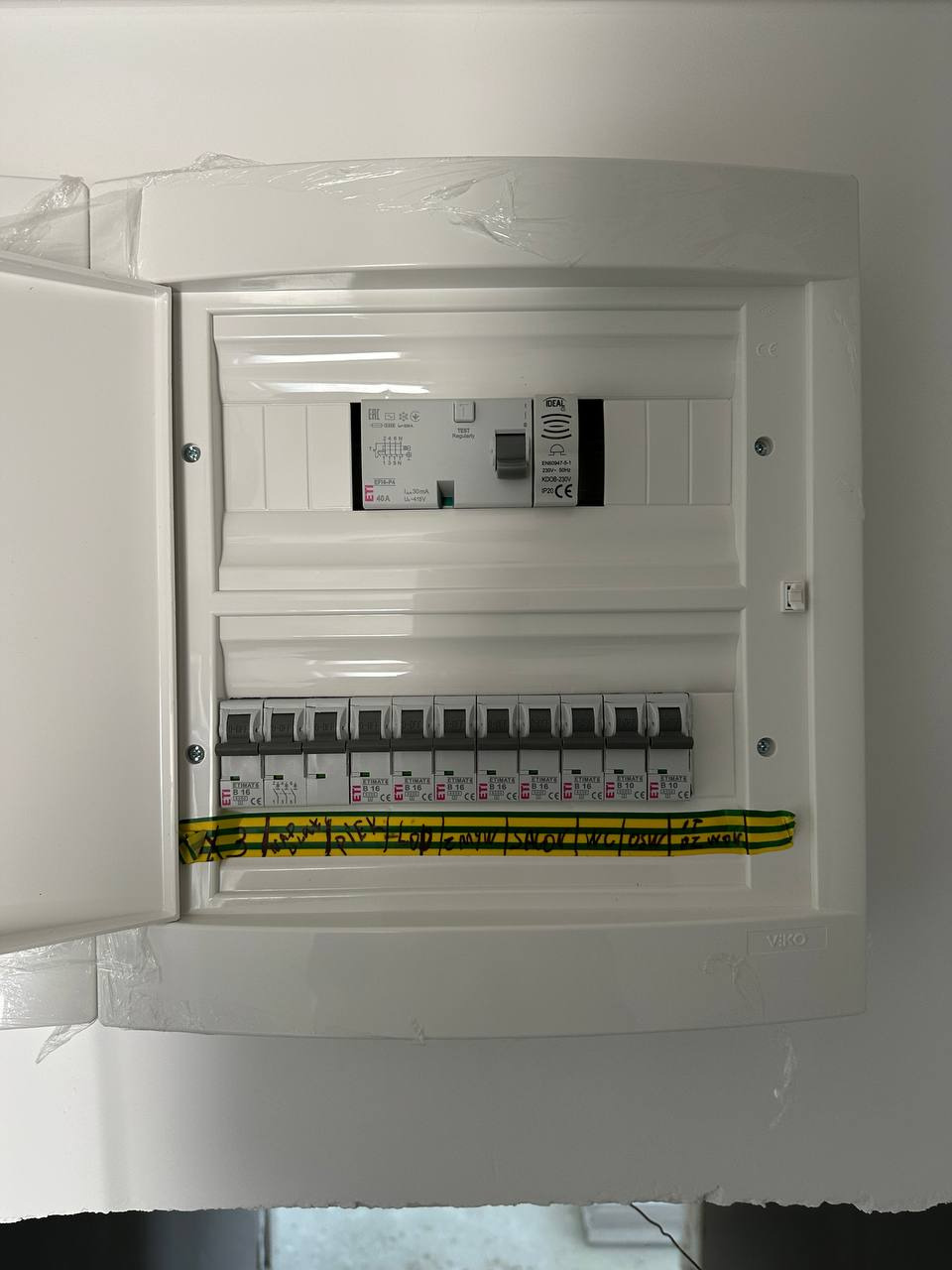 Otwarta, biała skrzynka rozdzielcza z zainstalowanymi bezpiecznikami ETI i napisem na przewodzie. Widoczny wyłącznik różnicowoprądowy.