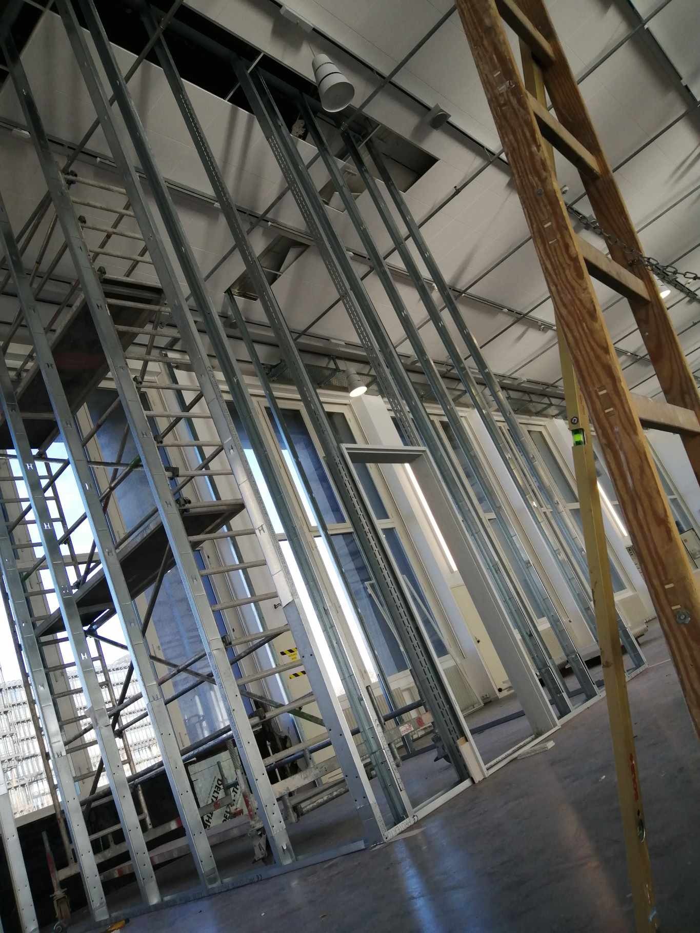 Konstrukcja szkieletowa ścian działowych z profili stalowych, widok z dołu, z fragmentem drewnianej drabiny po prawej stronie.