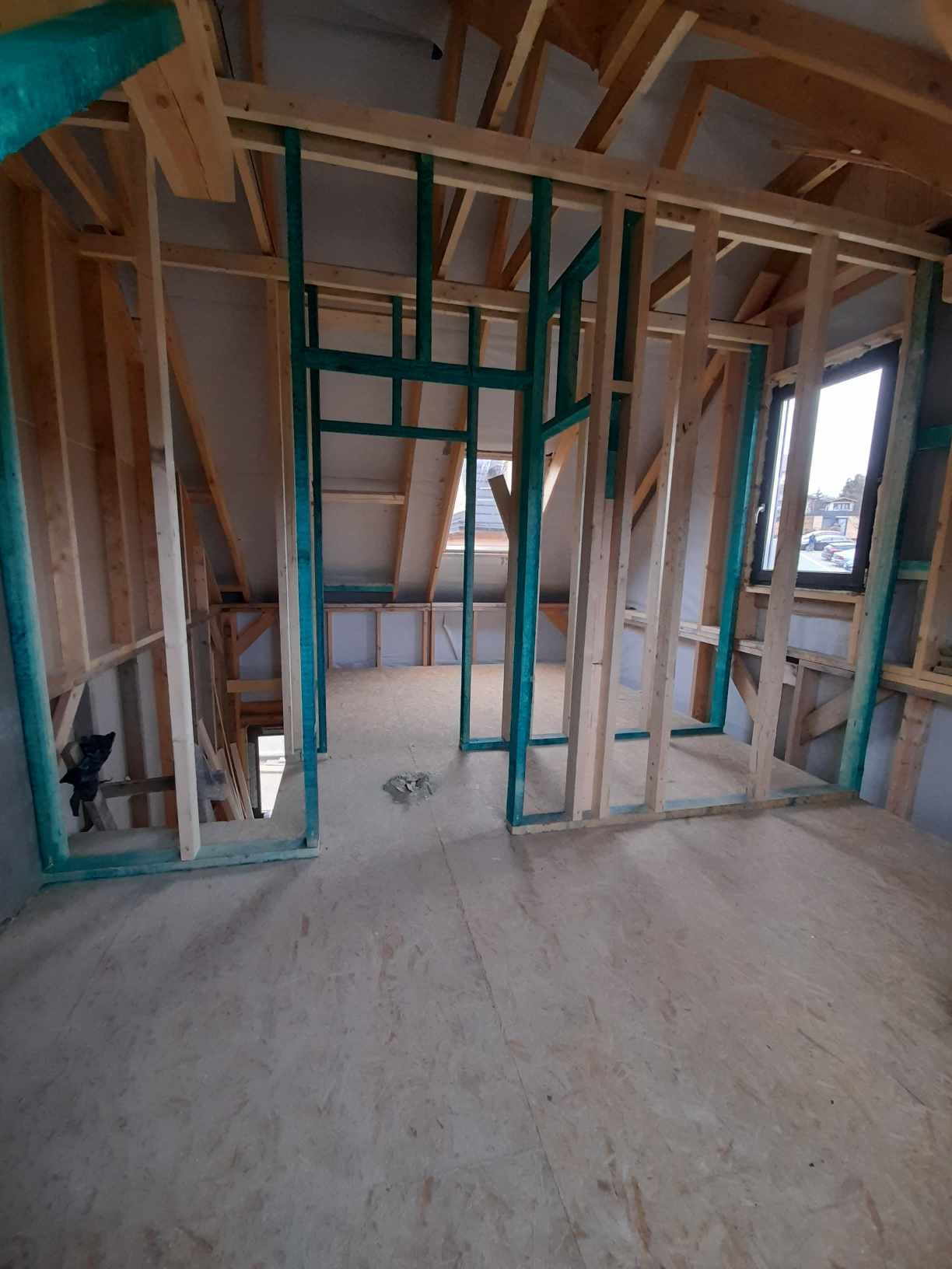 Szkielet ścian działowych z drewnianych belek, niektóre pomalowane na turkusowo, w trakcie adaptacji poddasza, widoczne okno i deski podłogowe.