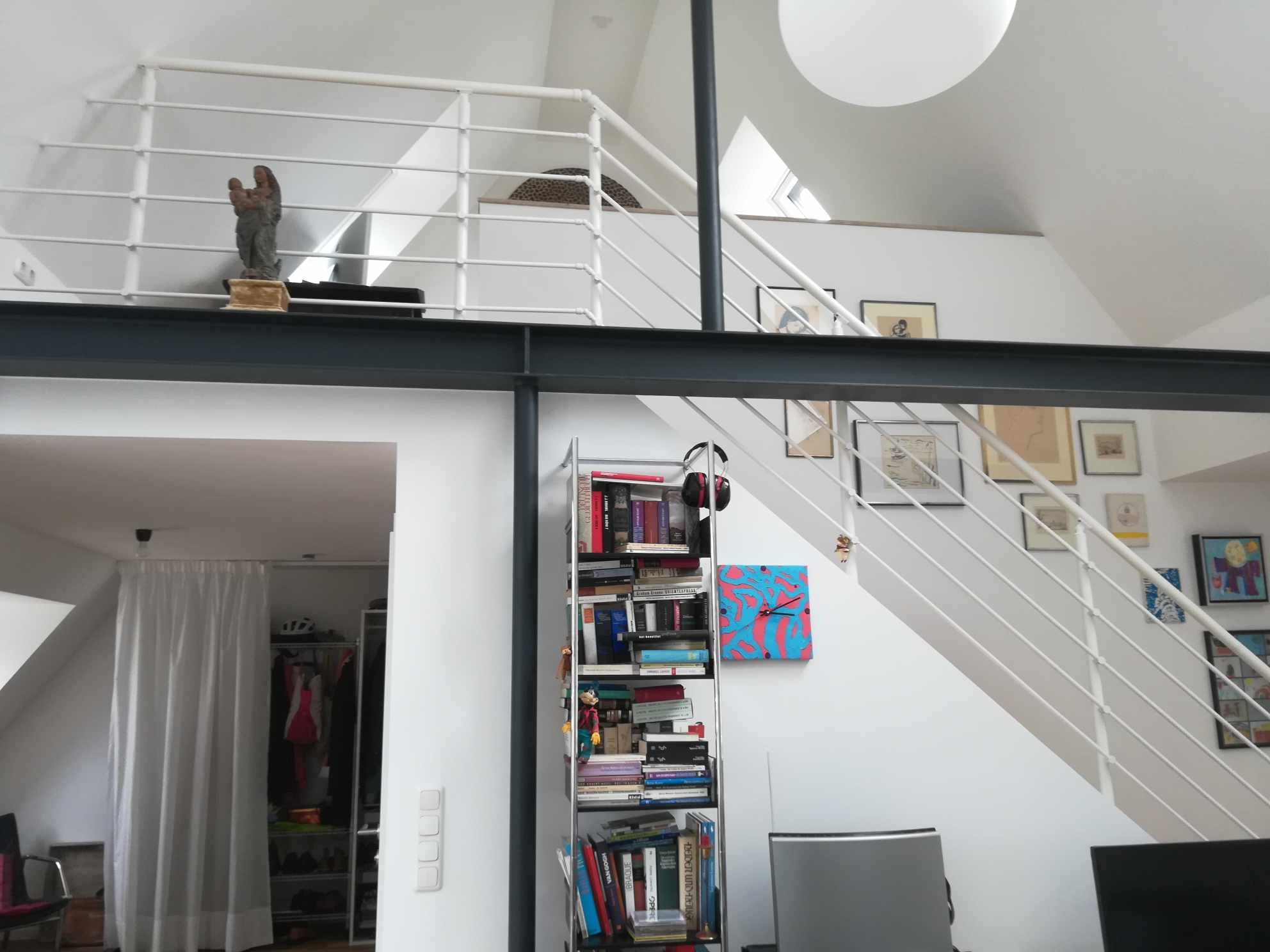 Wnętrze loftu z białymi schodami, antresolą i regałem na książki, widoczne elementy wykończenia i aranżacji wnętrz.