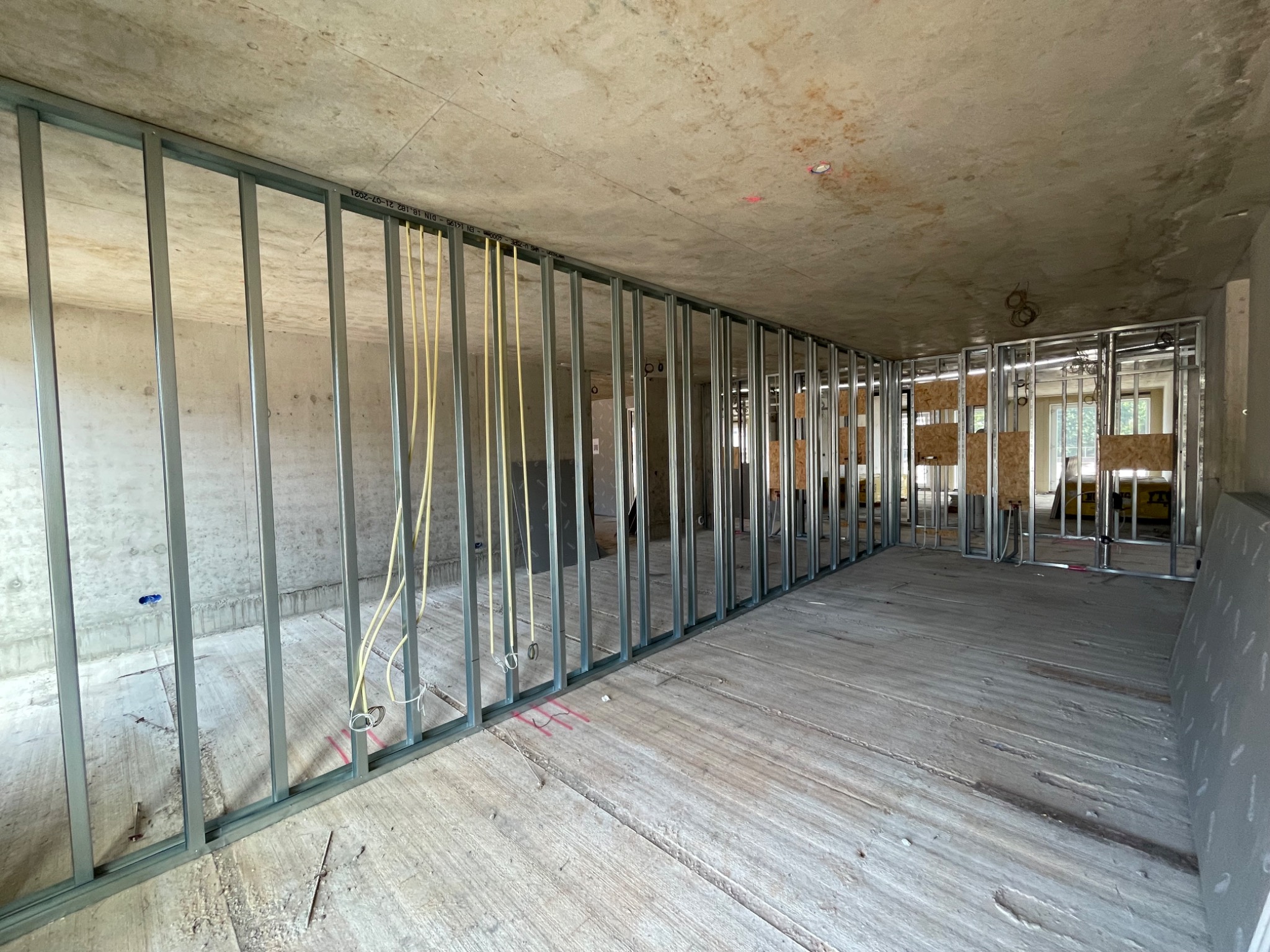 Metalowa konstrukcja szkieletowa ścian działowych w surowym wnętrzu, widoczne przewody elektryczne i fragmenty obudowy z płyt