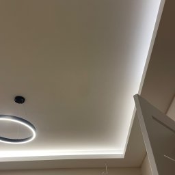 budmaxpainter Jakub Budnik - Nowoczesne oświetlenie sufitowe z wbudowanymi paskami LED i okrągłą lampą wiszącą, kremowe ściany, minimalistyczny design.