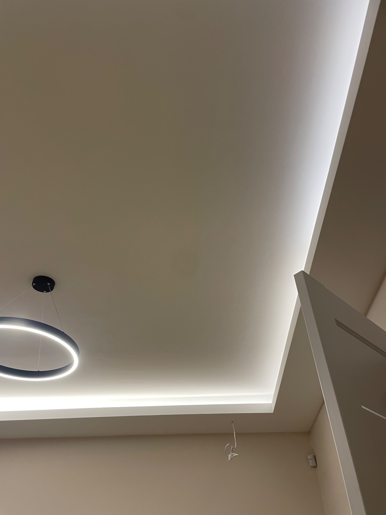 Nowoczesne oświetlenie sufitowe z wbudowanymi paskami LED i okrągłą lampą wiszącą, kremowe ściany, minimalistyczny design.